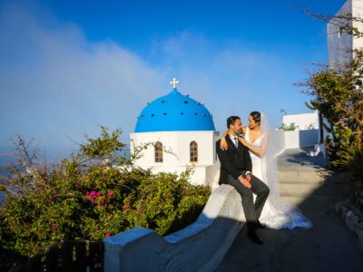 bride and groom portrait in front of a blue dome and caldera view, in Santorini island Greece. Elopement review